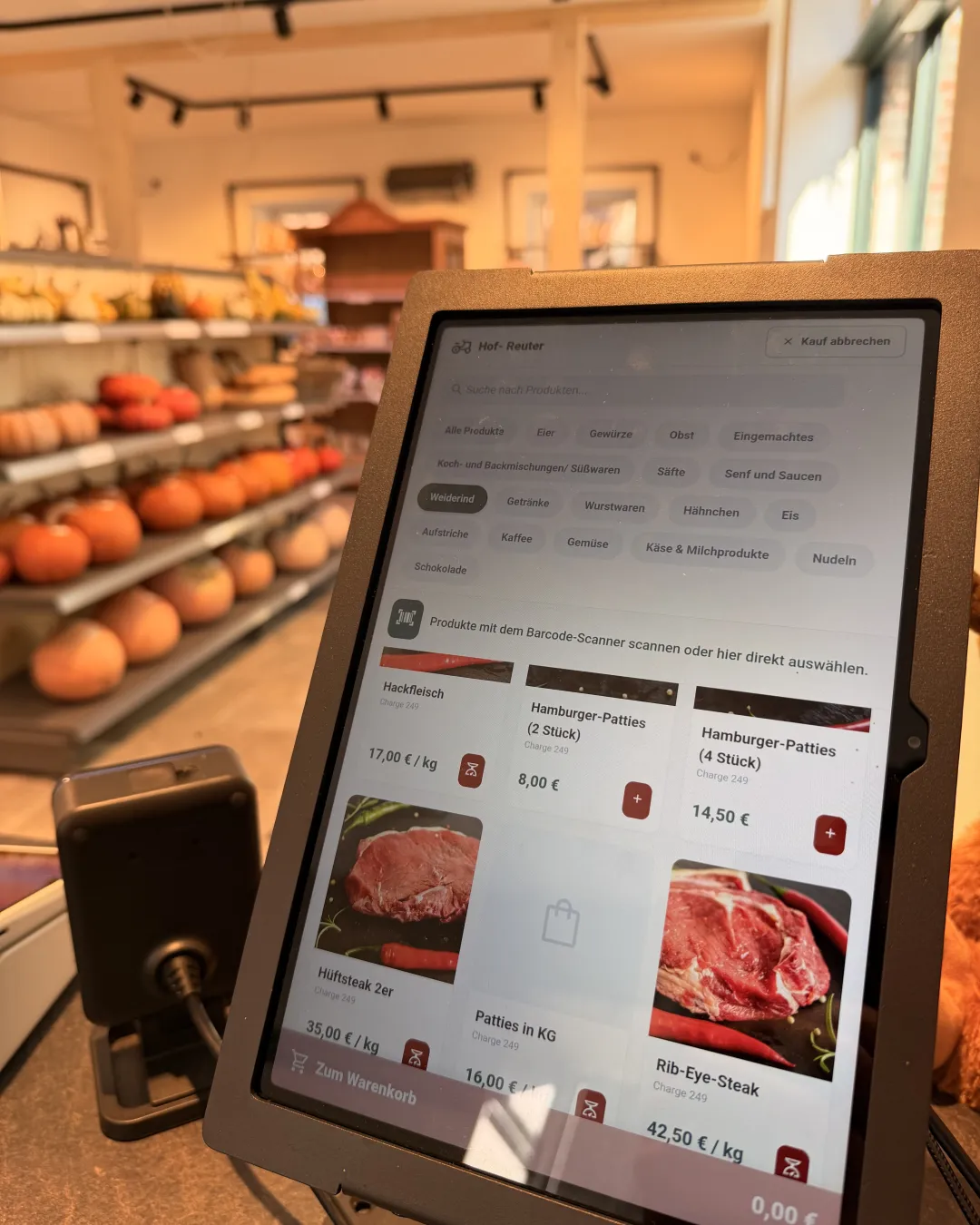 Die Self-Checkout-Kasse im Hofladen von Hof Reuter: Tablet mit Kategorien wie Weiderind, Eier und Eingemachtes, daneben der Barcode-Scanner, im Hintergrund Regale mit Kürbissen.